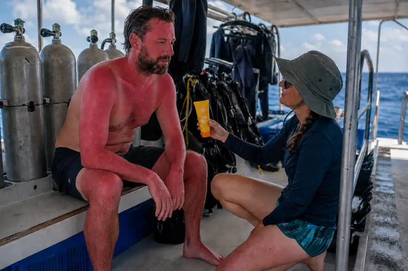 Sunburned diver on a liveaboard being offered reef-safe sunscreen