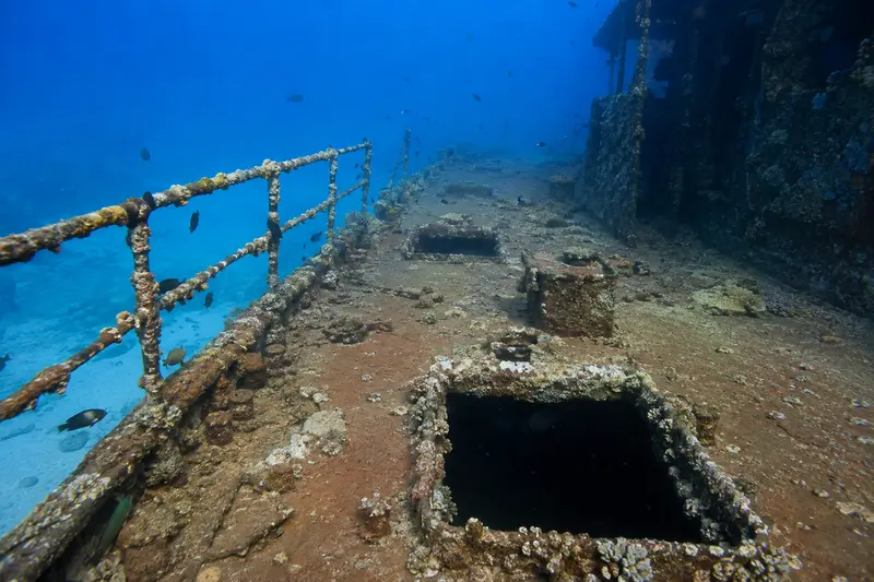 Corroded shipwreck deck with rails, hatch openings and reef growth in blue water
