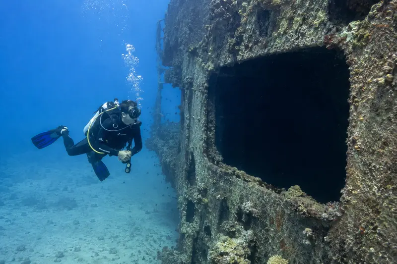 A scuba diver hovering outside a shipwreck opening without entering the wreck